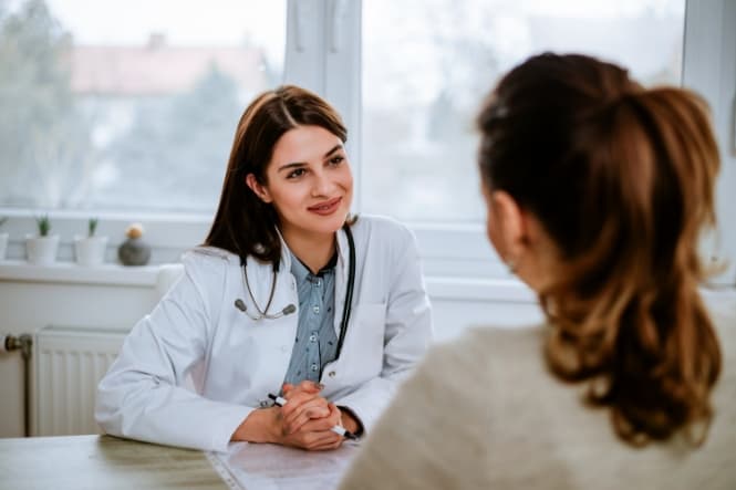 a female doctor seated across a desk from a female patient